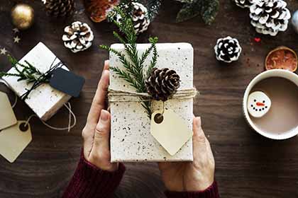 A photo showing two hands holding a wrapped gift with a few ornaments on the side