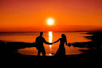 Couple holding hands in front of the sun.